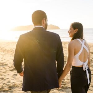 A couple walks hand in hand on a sunlit beach, capturing a romantic sunset moment.